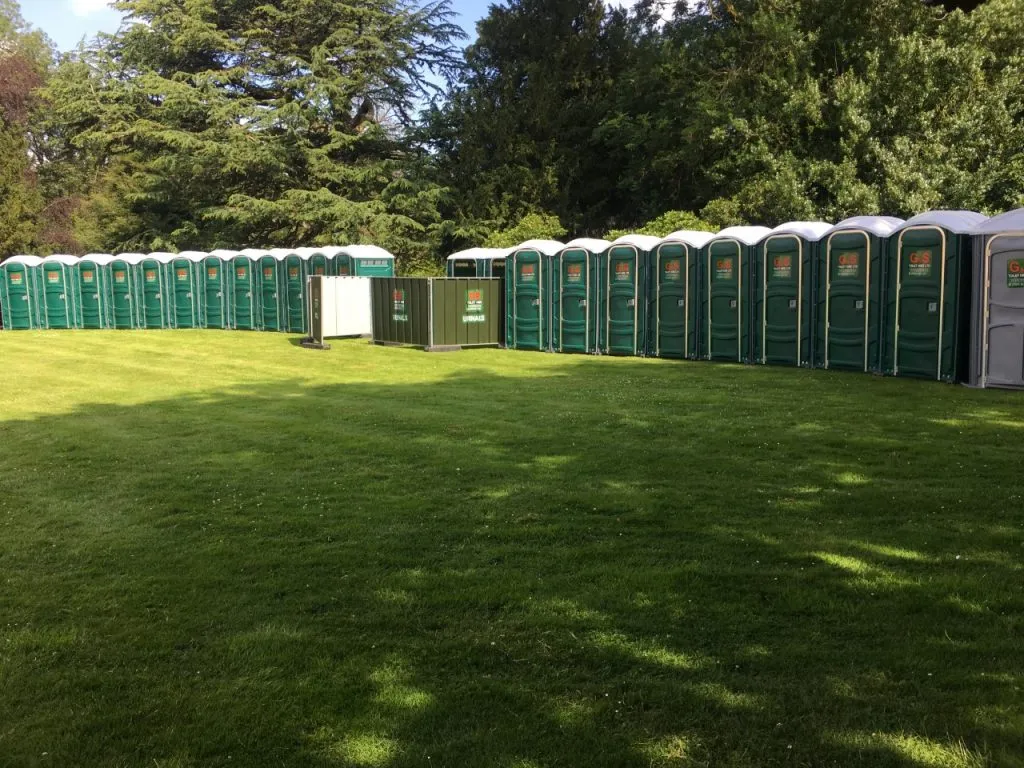 A long row of clean green G&S portable toilets set up on grass at an outdoor event