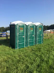 Three green G&S portable toilet units set up on grass at an outdoor event